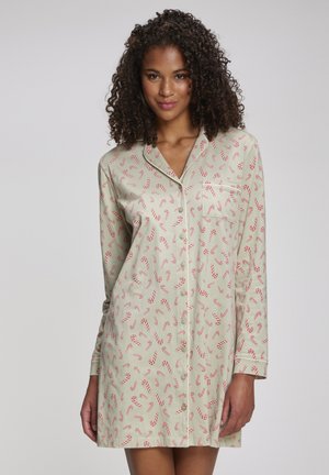 Woman with curly hair wearing a beige long-sleeve button-up nightshirt patterned with red and white candy canes.