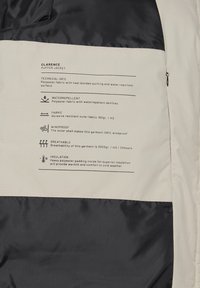 Puffer jacket with a black and cream color scheme, made from water-repellent polyester, featuring heat-bonded quilting and heavy padding.