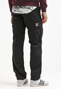 Pantalons cargo noirs avec poches latérales, fabriqués en tissu durable. Présentent une coupe décontractée et se marient bien avec des chaussures de sport grises.