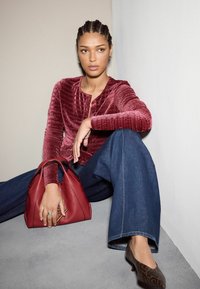 Burgunderfarbener strukturierter Oberteil mit rundem Ausschnitt, blaue weit geschnittene Jeans, rote Handtasche mit Doppelgriffen und braune gemusterte High Heels.