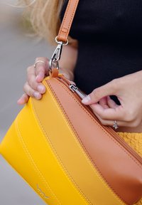 Žlutá a písečná kožená crossbody taška se zipovým uzávěrem, s texturovaným povrchem a stříbrným kováním. Její popruh je nastavitelný.