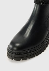 Stivaletto in pelle nera con punta tonda, suola antiscivolo texturizzata e dettaglio scintillante sulla parte superiore. Finitura liscia complessiva.