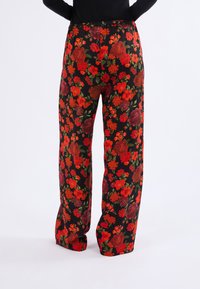 Pantalones de estampado floral con un fondo negro adornado con flores rojas y verdes. Elaborados en una tela ligera con un ajuste relajado y cinturilla elástica.
