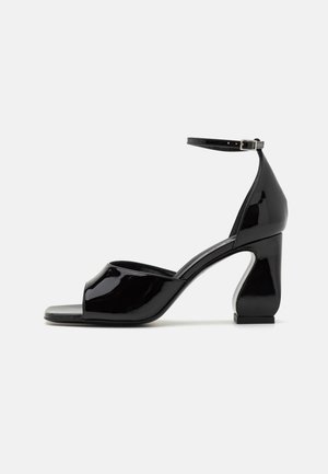 Mustad must kõrged kontsad avatud varbaga, ankle strap ja geomeetrilise chunky kontsaga. Sile, läikiv pind minimaalsete detailidega.