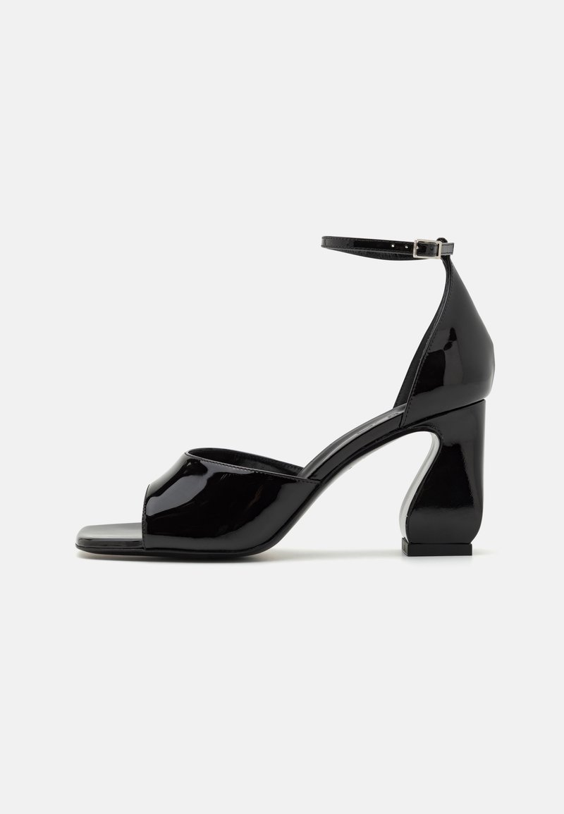 Μαύρες πατεντέ ψηλοτάκουνες σανδάλια με ανοιχτή μύτη, ιμάντα στον αστράγαλο και γεωμετρική χοντρή τακούνι. Λείο, λαμπερό επιφάνεια με ελάχιστες λεπτομέρειες.
