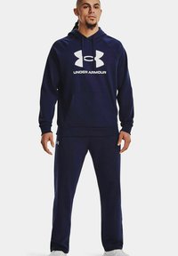 Completo felpa navy con cappuccio e pantaloni della tuta realizzato in tessuto morbido; presenta un grande logo bianco "Under Armour" e una tasca frontale sul cappuccio.