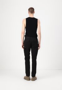 Svart tanktopp og bukser med cargo-funksjon, begge tettsittende, med to sidelommer og synlige sømdetaljer. Skoene har en tykk, robust såle.
