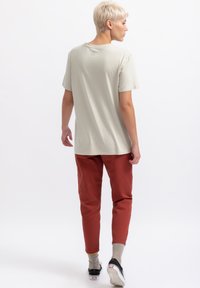 Lichtgrijze t-shirt met een relaxte pasvorm en korte mouwen, gecombineerd met roestkleurige tapered broeken en zwarte sneakers. Effen textuur, minimale details.