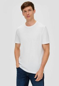 Weißes Baumwoll-T-Shirt mit kurzen Ärmeln und Rundhalsausschnitt, über dunkelblauen Jeans getragen. Einfaches, schlichtes Design ohne Muster.