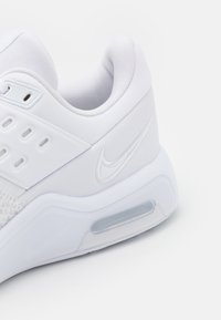 Biała sportowa półbuty z syntetyczną cholewką, wyściółką wokół kostki, poduszką powietrzną w pięcie oraz wytłoczonym logo z tyłu. Teksturowana podeszwa środkowa.