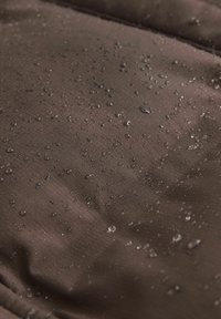 Tissu brun avec une texture lisse, montrant des gouttes d'eau sur la surface, indiquant des propriétés résistant à l'eau.