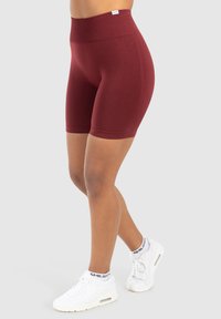 Bordeaux korte broek van rekbare stof, met een hoge tailleband en een zachte textuur, gecombineerd met witte sport sneakers.