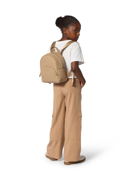 Zaino marrone con motivo a fantasia, dalla forma arrotondata, dotato di due spallacci regolabili e di una tasca frontale con cerniera. Abbinato a una maglietta bianca e pantaloni beige.