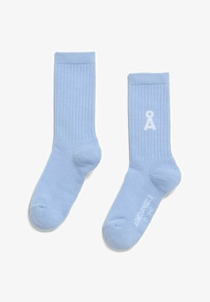 Hellblaue, gerippte Knöchelsocken, eine mit einem weißen Å-Logo nahe oben und die andere mit weißem Schriftzug „RHPDANGERS“ auf der Sohle.
