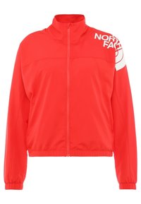 Röd zip-jacka i slät tyg med hög krage och elastiska ärmslut. "North Face"-logotypen tryckt i vitt på axeln.