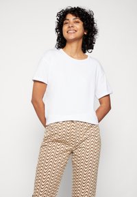 Camiseta branca de mangas curtas combinada com calças padrão em tom bege apresentando um design ondulado. O tecido parece suave e com um ajuste descontraído.