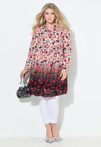 Abito floreale con motivi a cuore rossi e rosa, design a gradiente dal chiaro allo scuro, con maniche lunghe e vita arricciata. Abbinato a pantaloni bianchi.