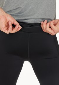 Schwarze Sportleggings mit glatter Oberfläche, hoch geschnittenem Bund und einer sichtbaren Reißverschlusstasche auf der Rückseite.