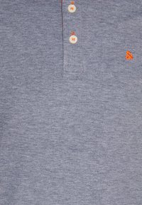 Polo gris texturé avec deux boutons blancs et un symbole esperluette orange brodé sur la poitrine.