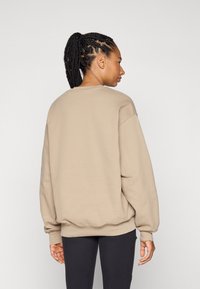 Beige oversized sweatshirt met lange mouwen, ronde halslijn en geribbelde manchetten, gecombineerd met zwarte legging, gezien vanuit de achterkant.