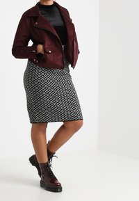 Giacca biker in similpelle scamosciata bordeaux, dolcevita aderente nero, gonna a matita con motivo bianco e nero, e stivali da combattimento bordeaux con lacci.