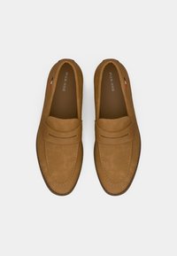 Smėlio spalvos zomšiniai mokasinai su lygiu paviršiumi, siuvinėtais elementais ir dviem horizontaliais dirželiais priekyje. Prekės ženklo logotipas matomas viduje.