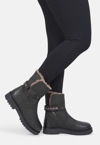 Czarne botki z ekoskóry z futrzanym wykończeniem, paskiem przy kostce i teksturowaną gumową podeszwą. Charakteryzują się płaskim obcasem i przeszyciami.