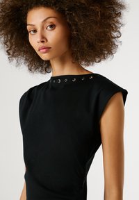 Top senza maniche di colore nero con un tessuto testurizzato, spalle strutturate e occhietti decorativi in argento lungo lo scollo.