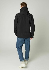 Czarna, wodoodporna kurtka z kapturem, o gładkiej teksturze i minimalistycznym designie. Noszona z podwiniętymi mankietami dżinsów i białymi trampkami.