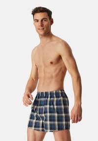 Mannen boxershorts met ruitpatroon in blauw, wit en grijs. Katoenen materiaal met een elastische tailleband en een relaxed fit. Patroonontwerp met geruite details.
