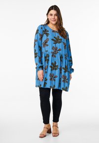 Blå blommig klänning med långa ärmar, samlad midja och svarta leggings. Har mörkbruna blommönster och ljusbruna öppna klackskor.