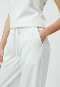 Pantaloni leggeri bianchi con vita elastica e tasche laterali, caratterizzati da una texture morbida e sottili righe verticali.