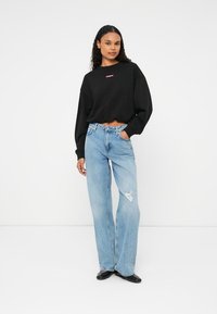 Pulover scurt negru cu guler rotund și logo roz, asortat cu blugi de denim ușor, bleu, cu găuri. Textură netedă, design relaxat.