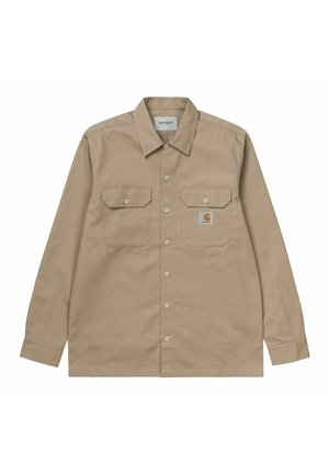Camicia beige a maniche lunghe con bottoni e due tasche sul petto, una delle quali presenta una toppa con il logo Carhartt.
