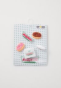 Jibbitz viehezis Krispy Kreme -teemasta valkoisella, pilkullisella kortilla, jossa on vaaleanpunainen ja suklaadonitsi, valkoinen laatikko ja logoteemat.