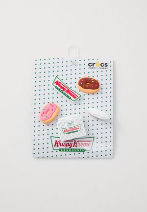 Charm del tema Krispy Kreme Jibbitz su una scheda bianca a pois, con una ciambella rosa e al cioccolato, una scatola bianca e accenti con il logo.