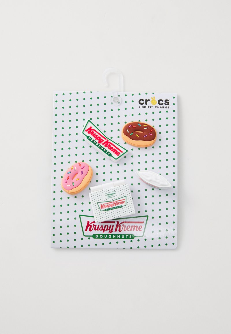 Charm del tema Krispy Kreme Jibbitz su una scheda bianca a pois, con una ciambella rosa e al cioccolato, una scatola bianca e accenti con il logo.