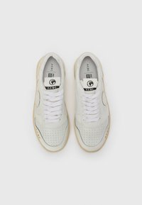 Sneaker in pelle bianca con design perforato, lacci piatti bianchi, suola in gomma color tanto e logo sulla linguetta e sul lato.