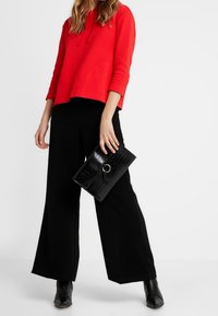Sudadera con capucha roja, de corte relajado, combinada con pantalones anchos negros. Clutch negro texturizado con detalle de hardware redondo. Botines negros.
