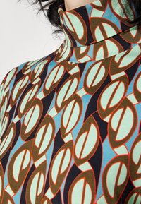 Turtleneck top met een herhalend patroon van ovale vormen in bruin, turquoise, rood en zwart op een lichte achtergrond. Soepele stof voor een comfortabele textuur.