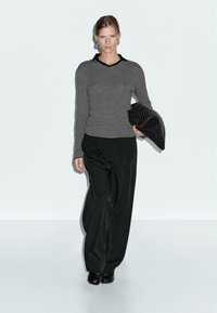 Black and white striped long-sleeve top with a v-neck, paired with loose black trousers. Holding a textured black clutch.