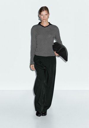 Black and white striped long-sleeve top with a v-neck, paired with loose black trousers. Holding a textured black clutch.