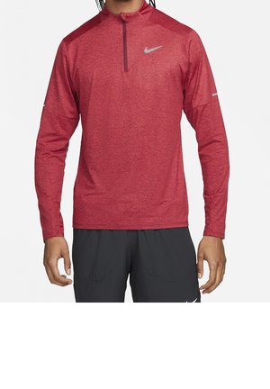Homme portant un haut de sport rouge à manches longues avec une fermeture éclair sur le quart supérieur et un petit logo Nike sur la poitrine, ainsi qu'un pantalon de sport noir.