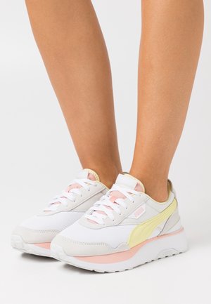 Weiße Sportschuhe aus Mesh- und Wildledermaterialien. Mit hellrosa Akzenten, gelbem Seiteneinsatz und dicker weißer Sohle.