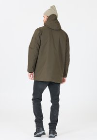 Olivgrön huppjacka i parka-stil, med en avslappnad passform, texturerad tyg och sidofickor, kombinerad med mörka jeans och grå skor.