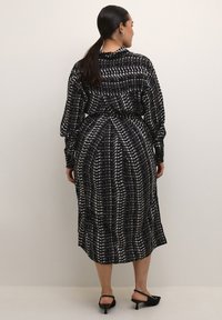 Abito midi a motivi in bianco e nero con maniche lunghe, vita cinchata e tessuto morbido e fluente. La vista posteriore mostra un design plissettato e una finitura liscia.