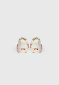 Baskets en toile blanches avec des bords effilochés et des accents rouges. La marque "DIESEL" est inscrite au talon, avec une tige basse et une forme arrondie.