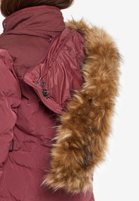 Chaqueta acolchada burdeos con cuello alto, con un ribete de piel sintética desmontable en la capucha y textura acolchada brillante.