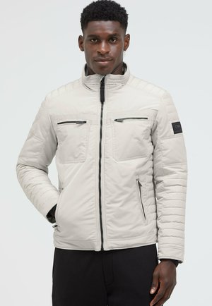 Helle graue gepolsterte Jacke mit Stehkragen, zwei Reißverschlusstaschen auf der Brust, seitlichen Taschen und gerippten Details an den Ärmeln.
