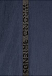 Tejido azul marino con un acabado texturizado, que presenta una franjas tejidas negras con la inscripción "WRONG FRIENDS" en letras brillantes, en vertical.